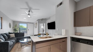 A modern kitchen with a central island, a dining area with a dark sofa, and a ceiling fan. - Central Relaxing 1br Phoenix Retreat Near Airport 1 Bedroom Apts (Phoenix)