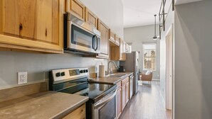 A modern kitchen with wooden cabinets, stainless steel appliances, and a long countertop. - Rustic-industrial Loft With Courthouse Views 3 Bedroom Apts (Bloomington)