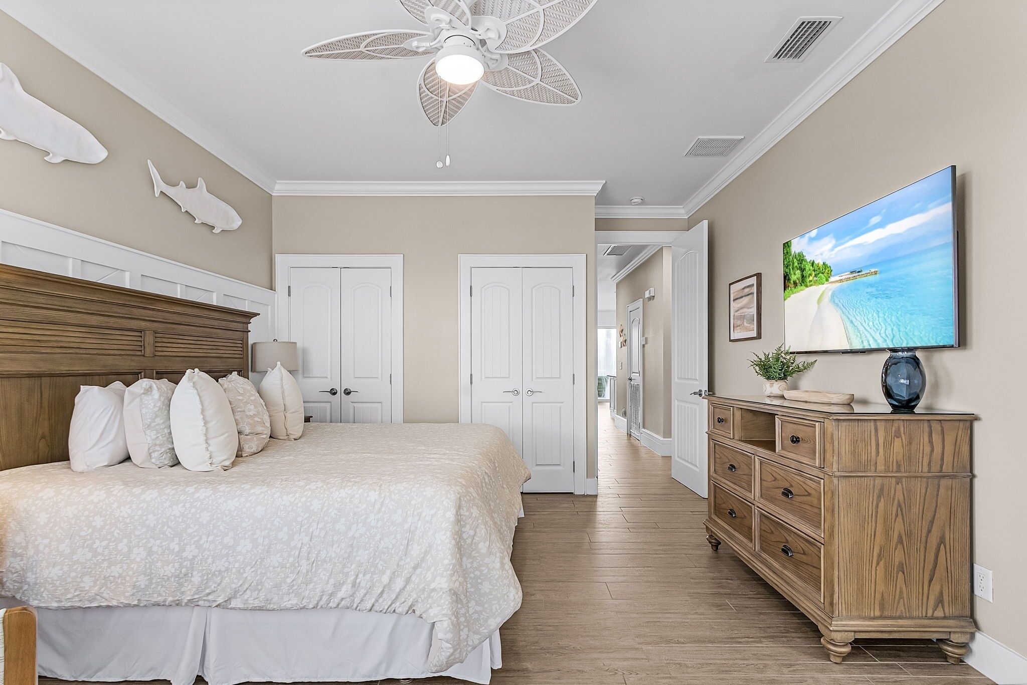 A bedroom with a bed, dresser, ceiling fan, and a TV on the wall.