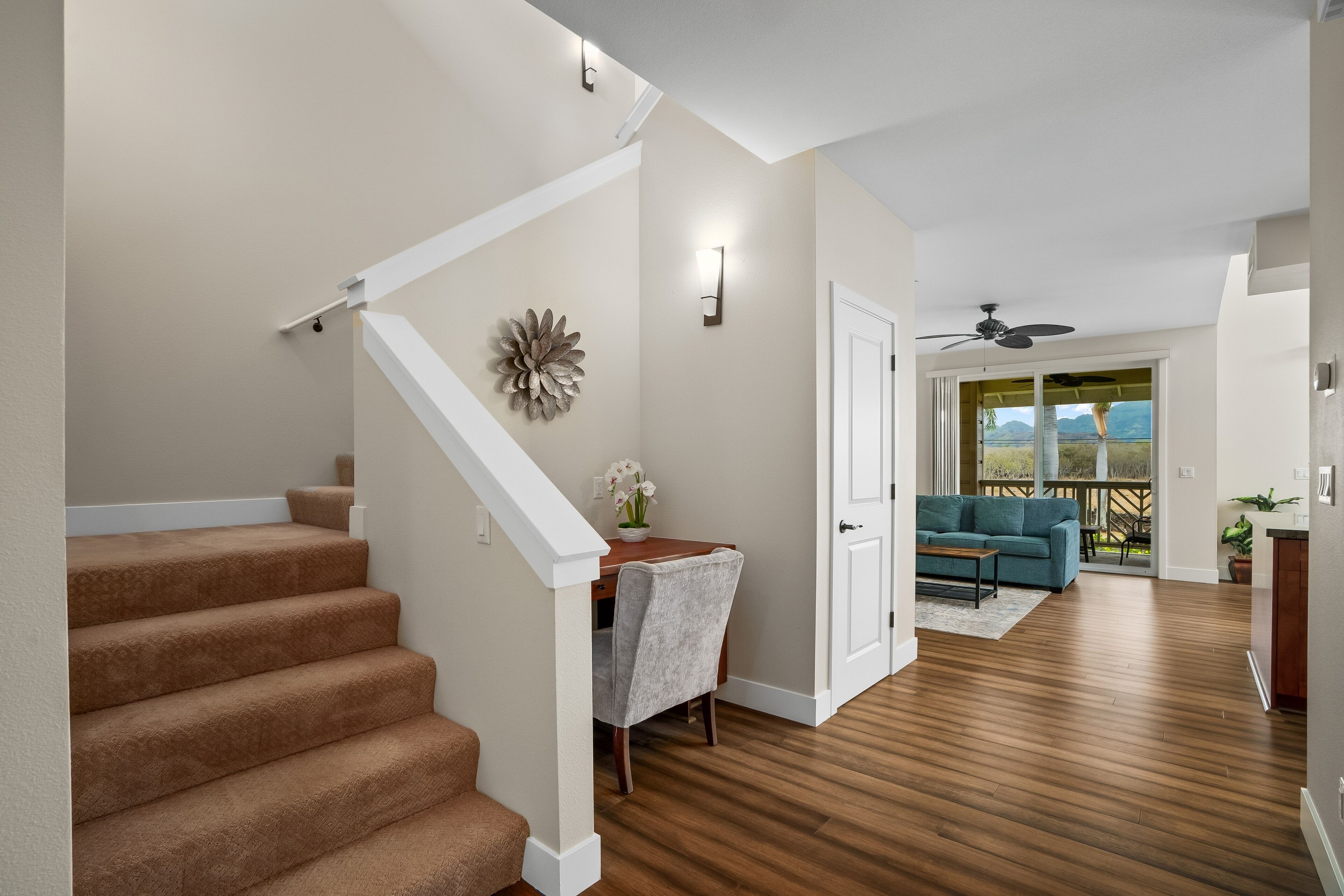 Un vaste espace de vie doté d’un plancher en bois, d’un escalier recouvert d’une moquette beige, d’une table à manger avec une chaise, et offrant une vue sur l’extérieur grâce à une porte-fenêtre coulissante.