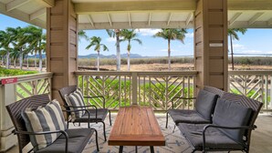 A covered patio with a wooden table and four chairs, overlooking a landscape with palm trees and distant mountains. - Kauai Pili Mai 14i 3 Bedroom Condo (Koloa)
