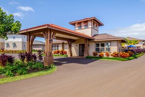 A two-story house with a covered patio, a driveway, and a well-maintained garden with various plants and flowers. - Kauai Pili Mai 14i 3 Bedroom Condo (Koloa)