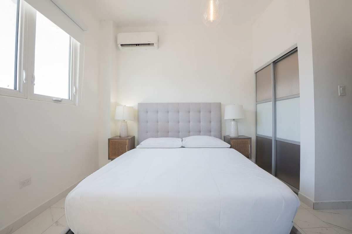 A hotel room with a large bed, two bedside tables with lamps, a sliding door closet, and an air conditioning unit on the wall.