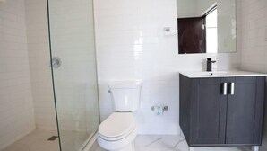 A bathroom with a glass shower enclosure, a white toilet, and a dark-colored vanity with a mirror above it. - Close To The Beach Apt. 71Di.203 (San Juan)