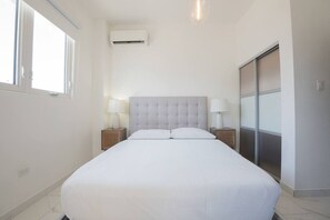 Ein Schlafzimmer mit einem Bett, zwei Nachttischen, einer Klimaanlage und einer Schiebetür.