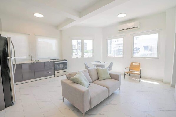 A modern living room with a sofa, a dining table, and a kitchen area.