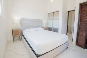 Ein Schlafzimmer mit Bett, Nachttischen, einem Kleiderschrank und einem durchgegangenen Tür sichtbaren Badezimmer.