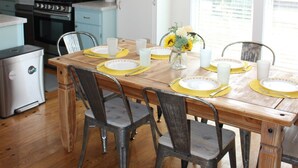 Una cocina moderna con una mesa de comedor dispuesta para cuatro, que incluye una araña, sillas de madera y un jarrón con flores.
