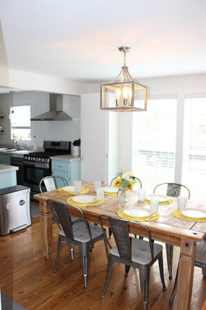 A modern kitchen with a dining table set for four, featuring a chandelier, wooden chairs, and a vase with flowers. - Peaceful lake front home with amazing views. (Middlesex)
