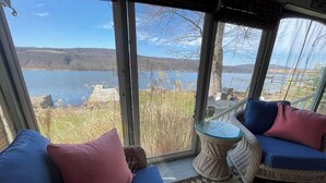 Una habitación con un gran ventanal con vistas al agua, mobiliario de mimbre y una alfombra estampada.