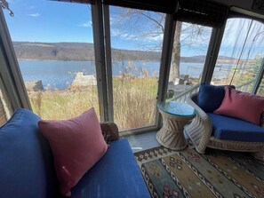 A room with a large window overlooking a body of water, wicker furniture, and a patterned rug. - Peaceful lake front home with amazing views. (Middlesex)