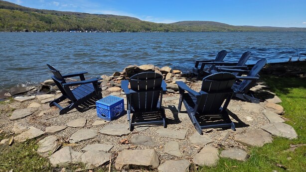 Un entorno junto al lago con sillas Adirondack y un canasto azul sobre un área empedrada.