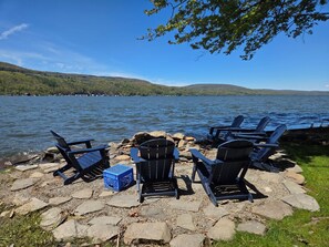A lakeside setting with Adirondack chairs and a blue crate on a stone-paved area. - Peaceful lake front home with amazing views. (Middlesex)