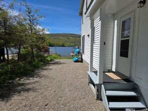A gravel path leading to a house with a porch, a dock, and a lake view. - Peaceful lake front home with amazing views. (Middlesex)