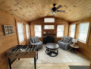 A cozy room with wooden walls, a foosball table, two sofas, a fireplace, and a ceiling fan. - Peaceful lake front home with amazing views. (Middlesex)