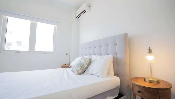 A bedroom with a bed, a bedside table, a lamp, and a window.