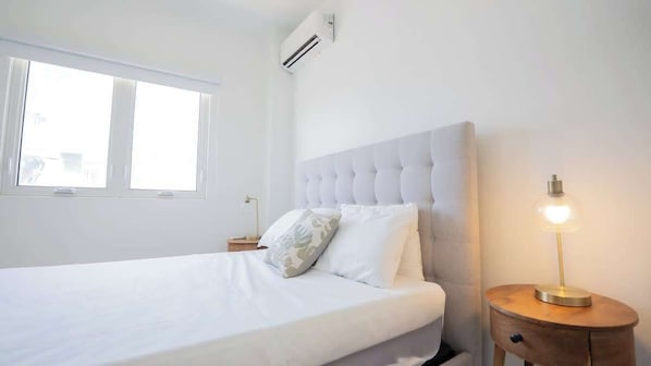 Un dormitorio con cama, mesita de noche, lámpara y ventana.