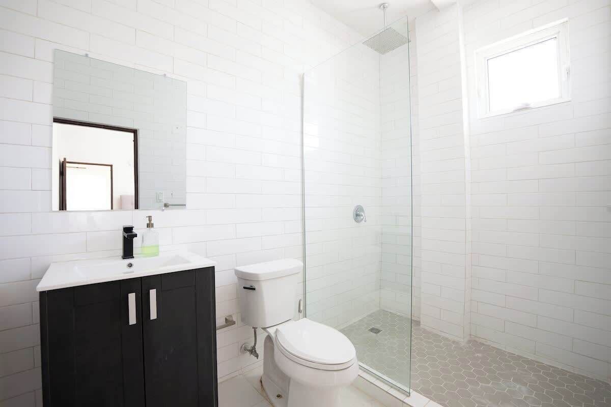 A modern bathroom with a white tiled wall, a black cabinet, a white toilet, and a glass-enclosed shower area.