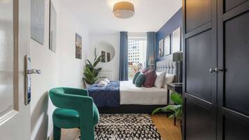 A bedroom with a bed, a green chair, a black and white patterned rug, and a dark wardrobe.