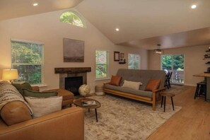 A living room with a fireplace, a sofa, a coffee table, and a dining area. - NEW hot tub at this escape for 8! (Ashford)