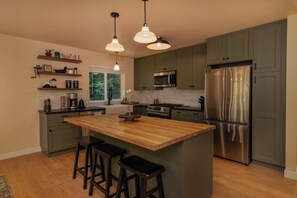 Een moderne keuken met een centraal eiland, barkrukken, roestvrijstalen apparatuur en groene kastjes.