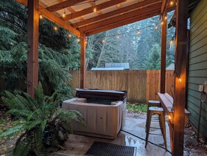 A covered outdoor area with a hot tub, wooden benches, and string lights. - NEW hot tub at this escape for 8! (Ashford)
