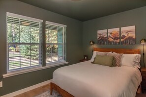 A bedroom with a bed, two windows with blinds, a nightstand, a lamp, and wall art. - NEW hot tub at this escape for 8! (Ashford)