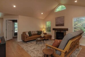 Een woonkamer met een bank, fauteuil, open haard en een deur naar een andere kamer.