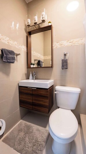 A bathroom with a white toilet, a wooden vanity with a mirror, and a small rug on the floor.