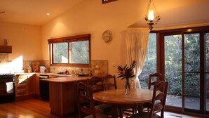 Une cuisine avec un îlot central en bois, une table à manger et des chaises, de grandes fenêtres avec des rideaux et un luminaire suspendu.