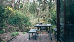 Une terrasse en bois avec une table et des bancs, entourée d’une végétation luxuriante et d’arbres.