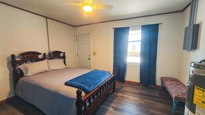A bedroom with a bed, a ceiling fan, a window with curtains, a bench, and a water heater.