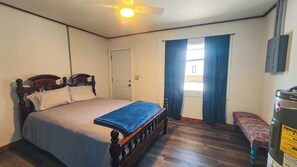 A bedroom with a bed, a ceiling fan, a window with curtains, a bench, and a water heater.