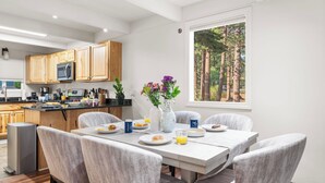 Eine moderne Küche mit Holzausstattung, einem Esstisch mit sechs Stühlen und einem großen Fenster mit Blick auf einen Wald.