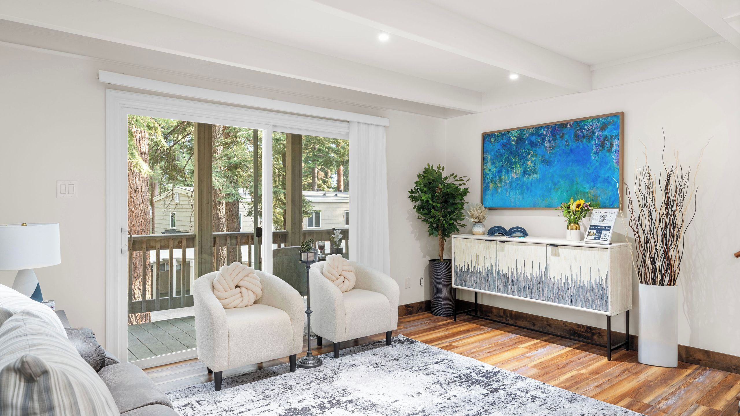 A living room with a sofa, two armchairs, a coffee table, a painting, and a view through the glass door.