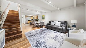 Ein modernes Wohnzimmer mit einer Holztreppe, einem Essbereich und einer Küche im Hintergrund.