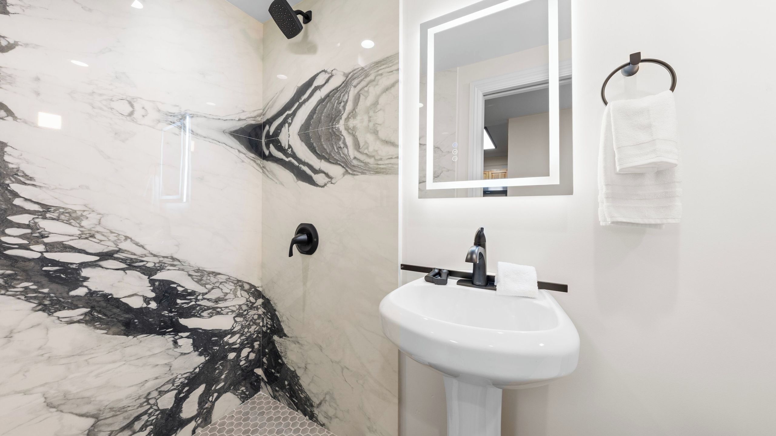 A bathroom with a marble wall, a sink, a mirror, and a towel rack.
