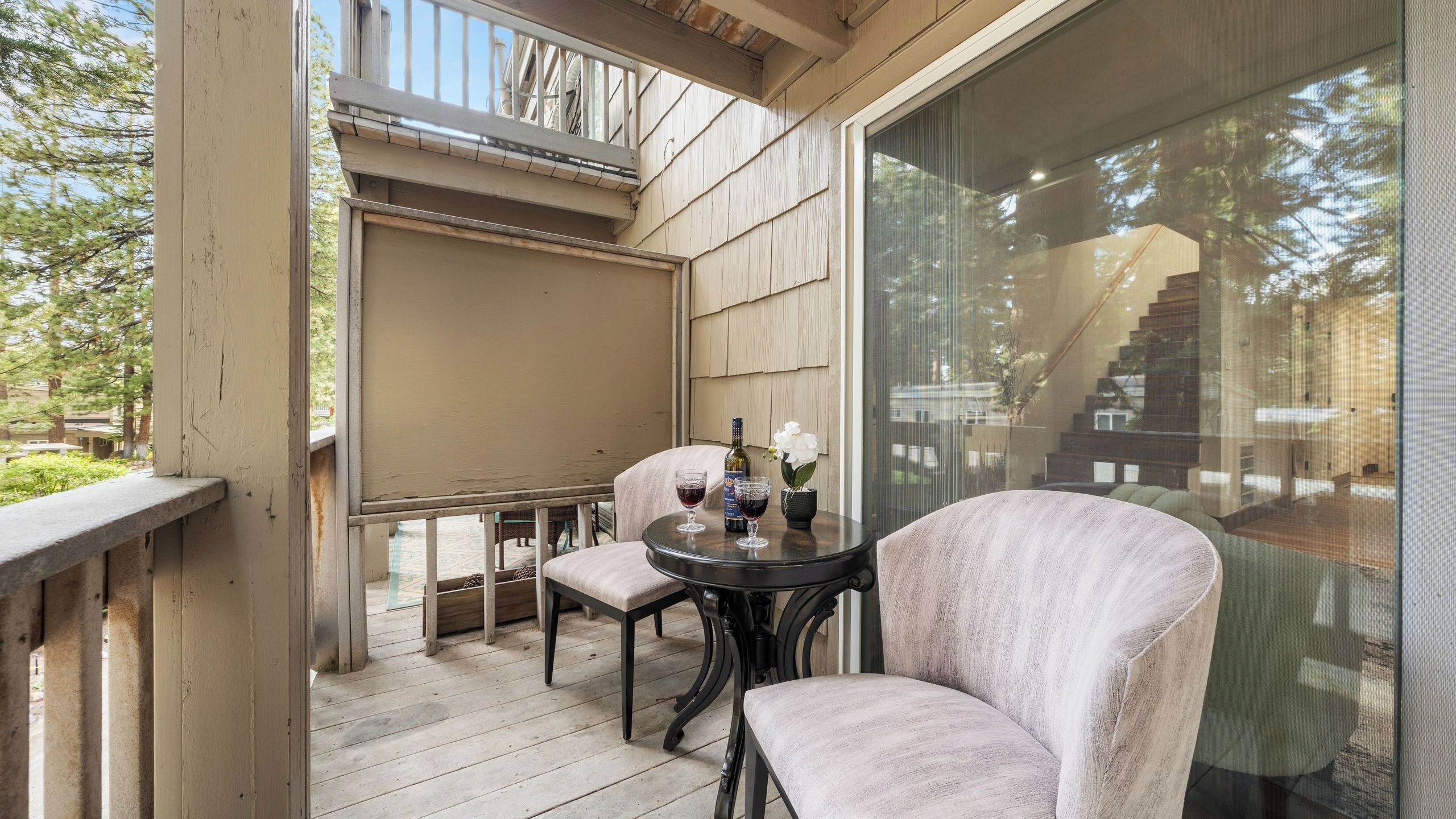 A covered outdoor seating area with a table, two chairs, and a bottle of wine.