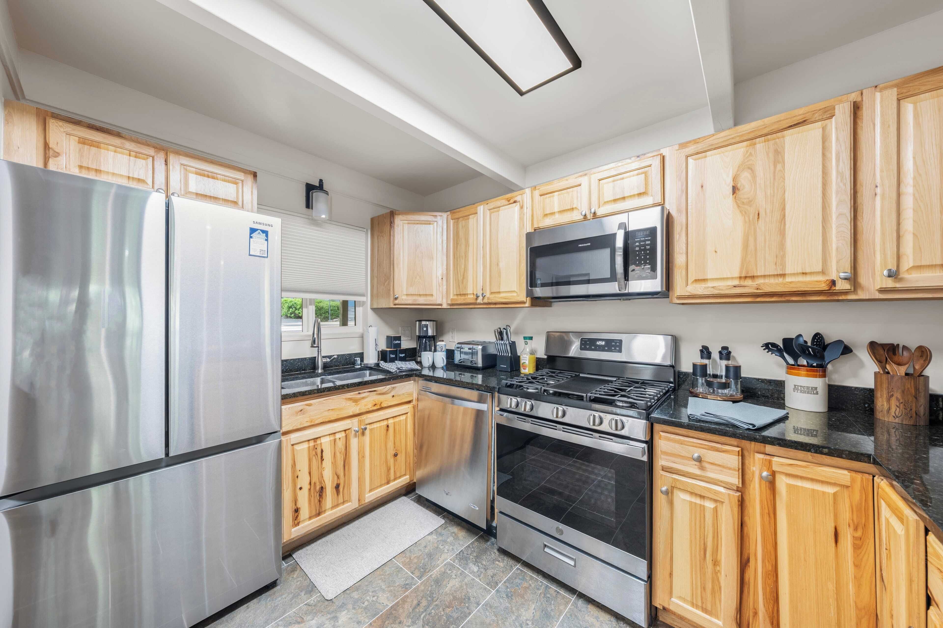 A modern kitchen with stainless steel appliances, wooden cabinets, and a large window.