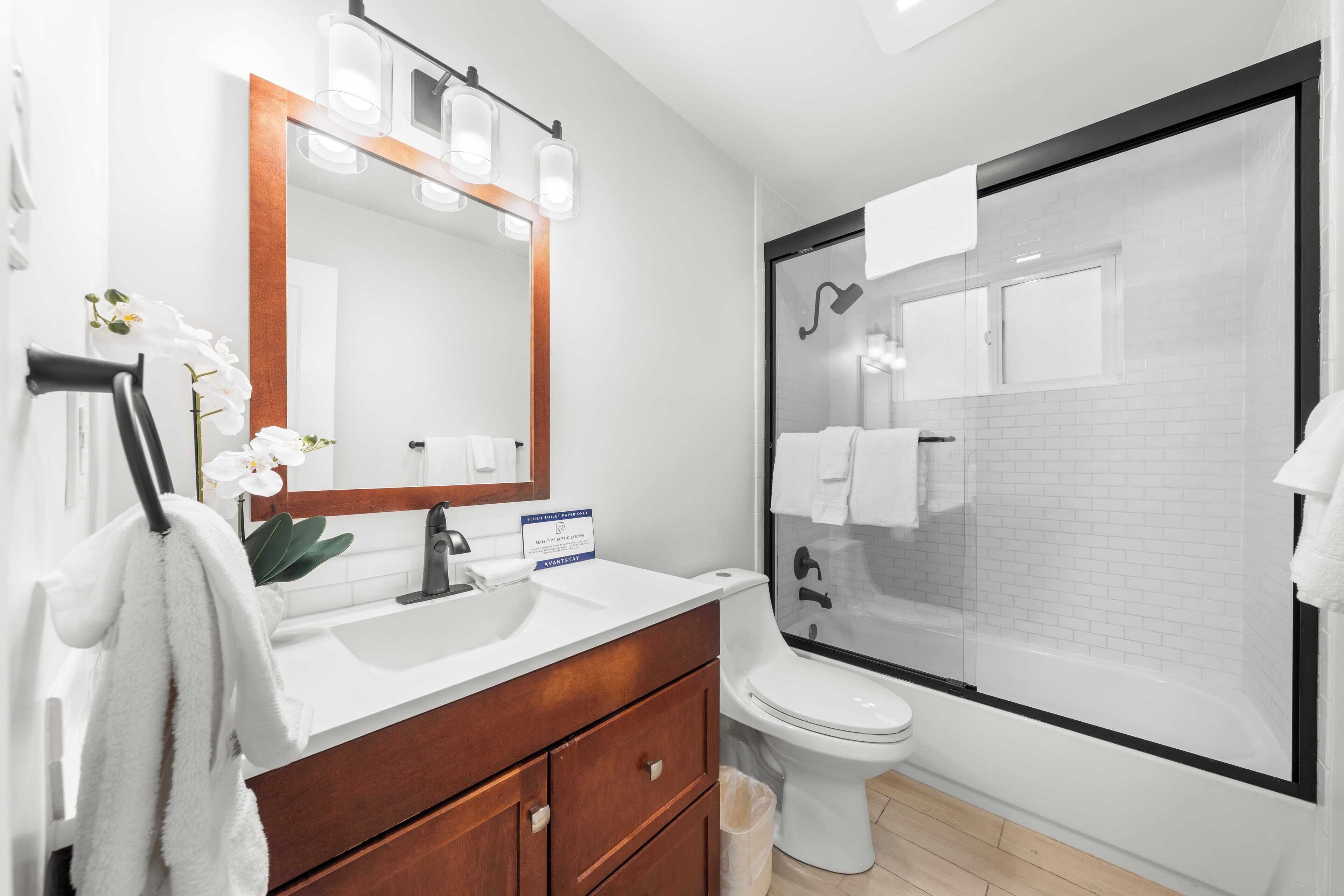 A modern bathroom with a white sink, wooden vanity, a large mirror, and a glass-enclosed shower.