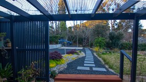 A wooden deck with a metal pergola and a garden path leading to a house. - The Orchard - Cosy A-Frame Mountain Hideaway (Leura)