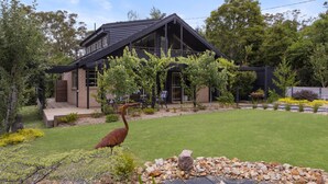 A modern house with a sloped roof, large windows, and a well-maintained garden with a pond and a bird. - The Orchard - Cosy A-Frame Mountain Hideaway (Leura)