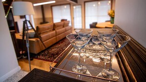 A modern living room with a glass coffee table holding martini glasses, a sofa, and a lamp. - The Orchard - Cosy A-Frame Mountain Hideaway (Leura)