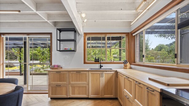 A modern kitchen with wooden cabinets, a large window, and a view of greenery outside. - The Orchard - Cosy A-Frame Mountain Hideaway (Leura)