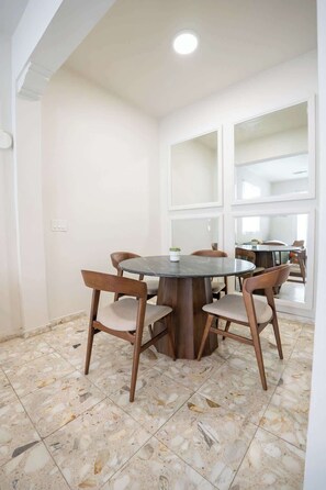 Uma sala de jantar com uma mesa redonda e quatro cadeiras, uma luminária no teto e piso de azulejos.
