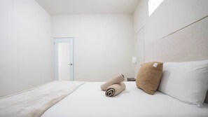 Una habitación de hotel con cama, una puerta y una mesita de noche con lámpara.