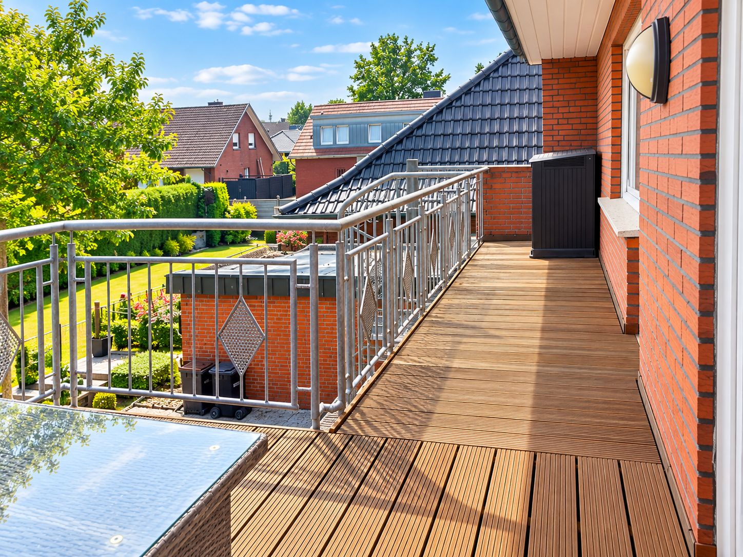 A wooden deck with a metal railing, a black outdoor heater, and a brick wall.