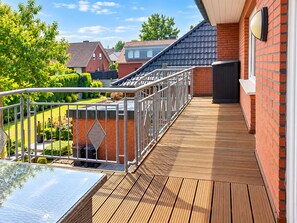 Une terrasse en bois avec une rambarde en métal, un chauffage d’extérieur noir et un mur en briques.