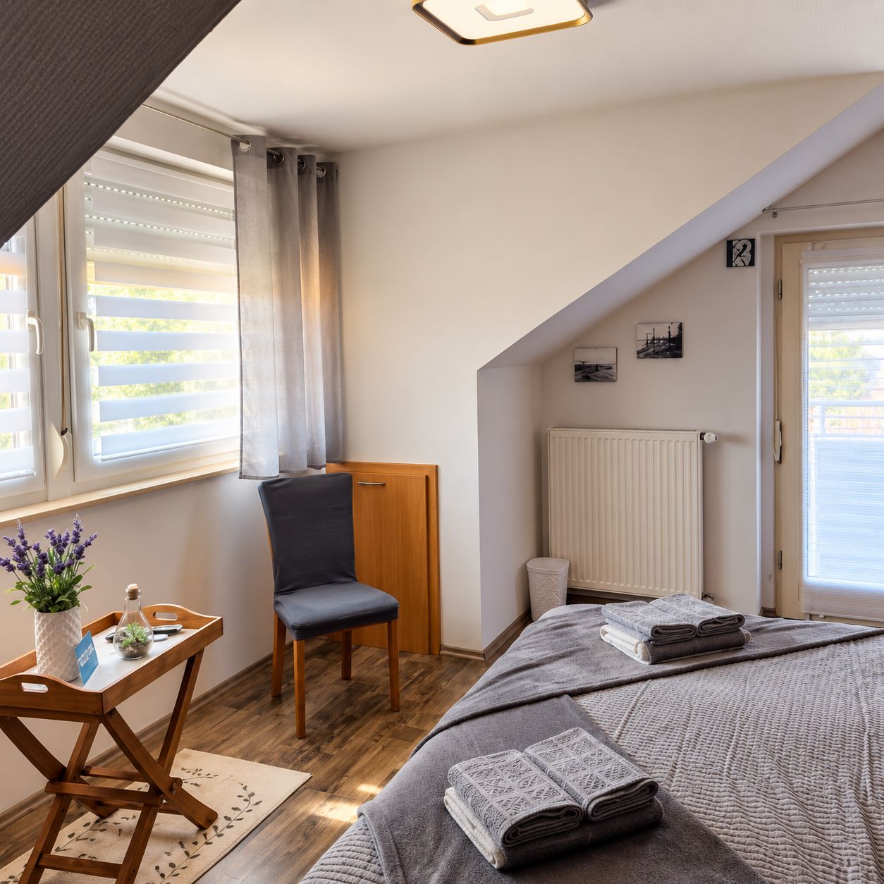 A bedroom with a bed, a chair, a small table with a vase, and a radiator.