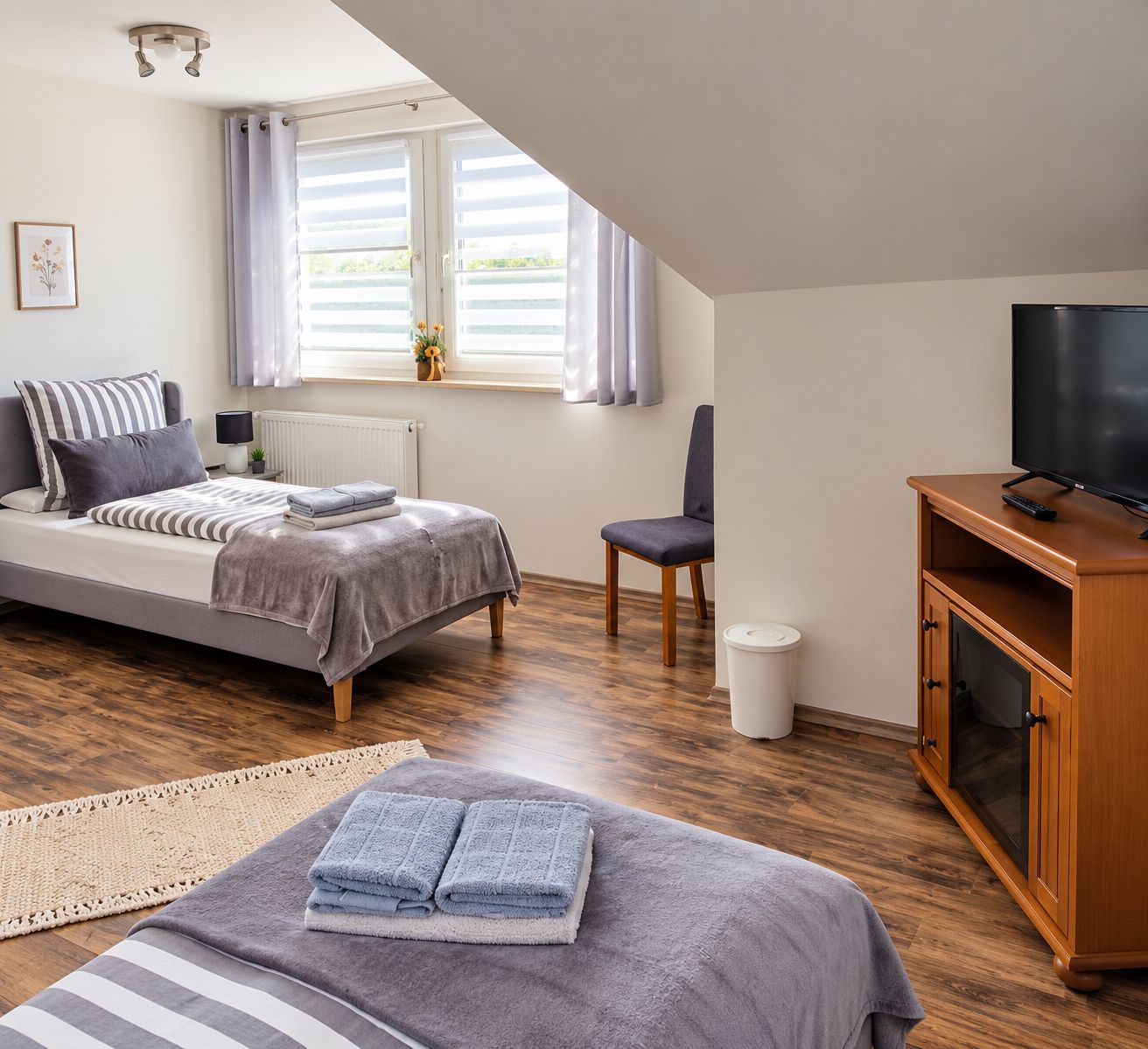 A bedroom with a bed, a chair, a TV, and a window with curtains.